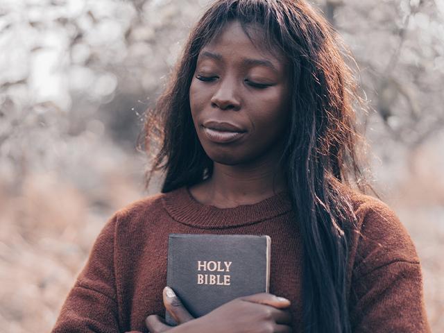 woman holding Bible across her chest with her eyes closed