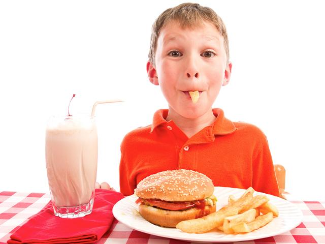 young boy eating a french fry with a chocolate milk shake