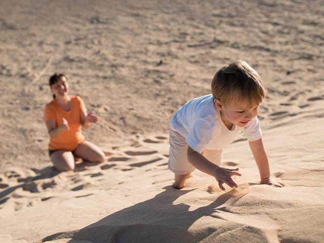 boy climbing a sand dune with his mother at the base of it encouraging him