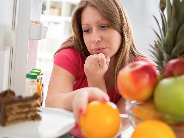 woman looking in the refrigerator at cake and fruit