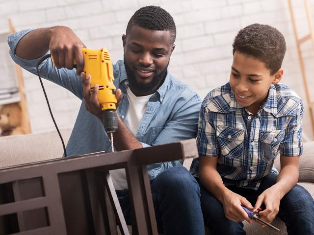 dad using a drill and son watching while holding a tool