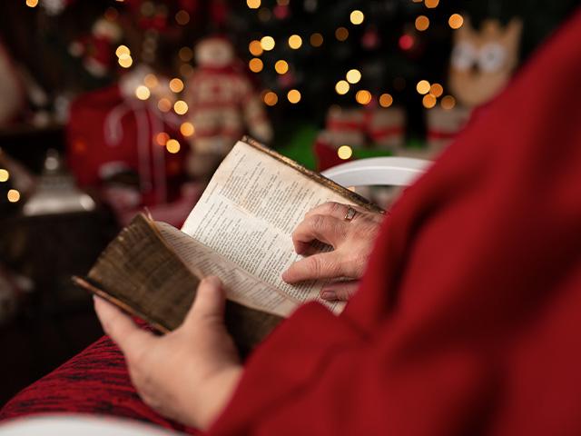 senior person sitting near christmas tree reading the Bible