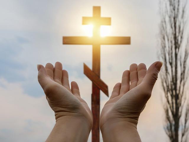 hands opening to a cross in the sunny sky