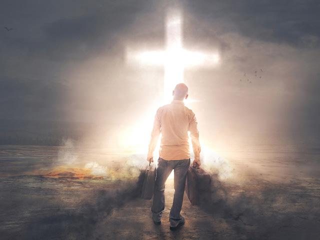 a man walking through darkness heading to light coming from a cross