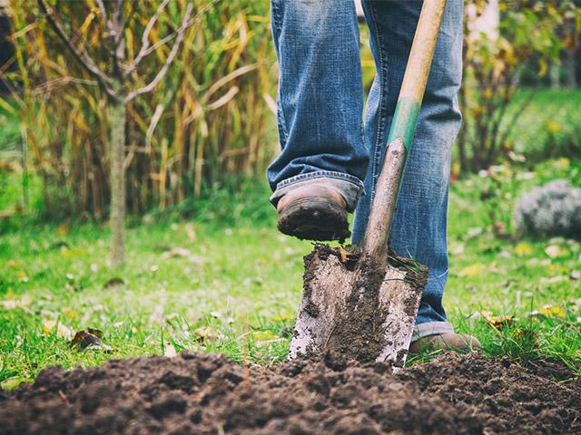 a foot pressing a shovel into the mud