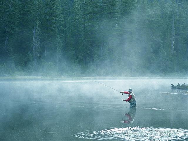 fog over a lake with a man fishing in waders