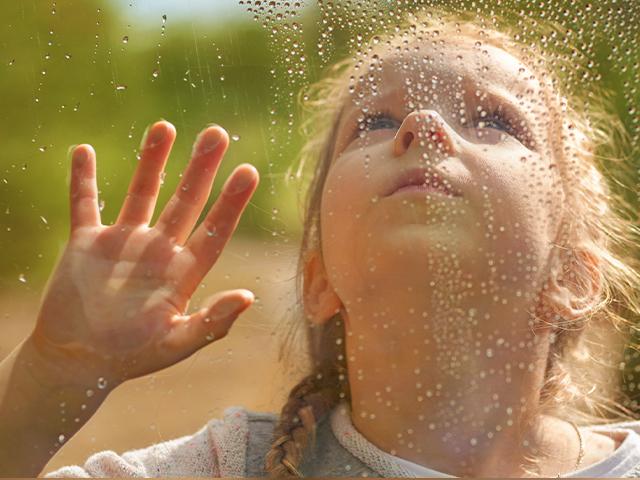 girl watching water droplets roll down a window