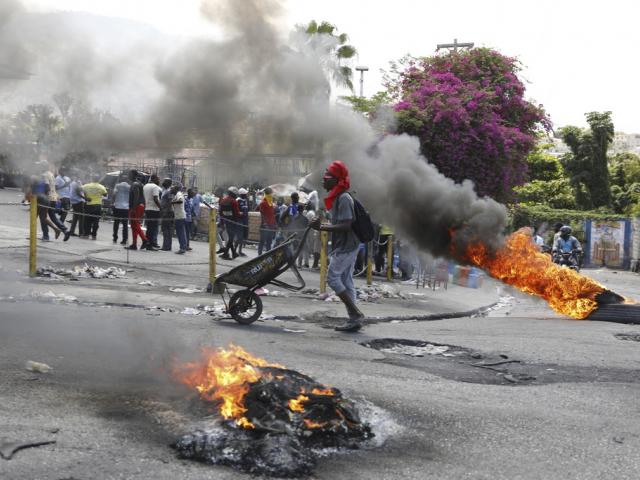 A man pushes a wheelbarrow past burning tires during a protest demanding the resignation of Prime Minister Ariel Henry, in Port-au-Prince, Haiti, Thursday, March 7, 2024. (AP Photo/Odelyn Joseph)