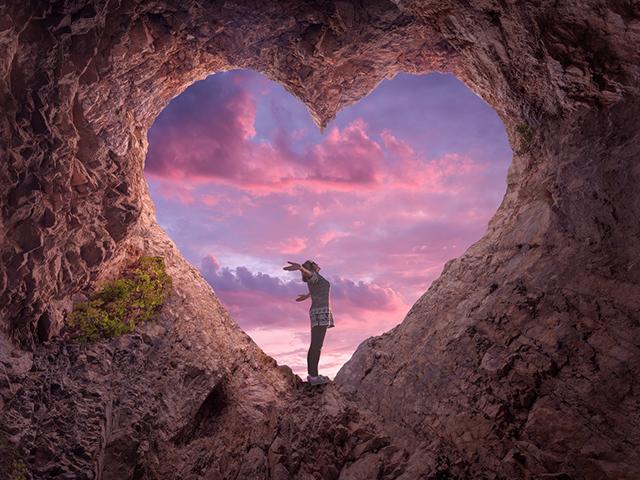 woman praising God in a heart-shaped cave opening