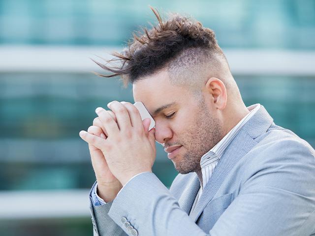 man with eyes closed praying and hoping with his phone to his head