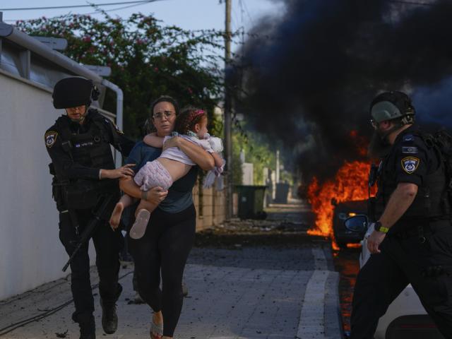 Police officers evacuate a woman and a child from a site hit by a rocket fired from the Gaza Strip, in Ashkelon, southern Israel, Saturday, Oct. 7, 2023. The rockets were fired as Hamas announced a new operation against Israel. (AP Photo/Tsafrir Abayov)