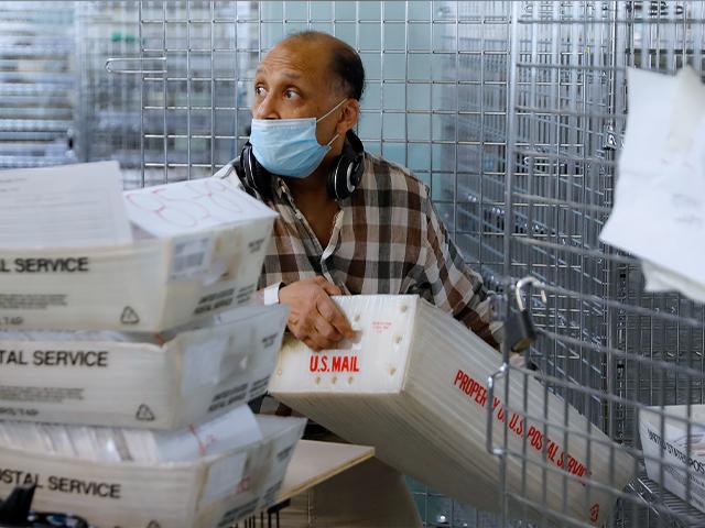 A worker gathers ballots from security cages before they are checked at a Board of Elections facility, Wednesday, July 22, 2020, in New York. (AP Photo/John Minchillo)