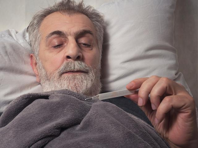 man in bed looking at a thermometer