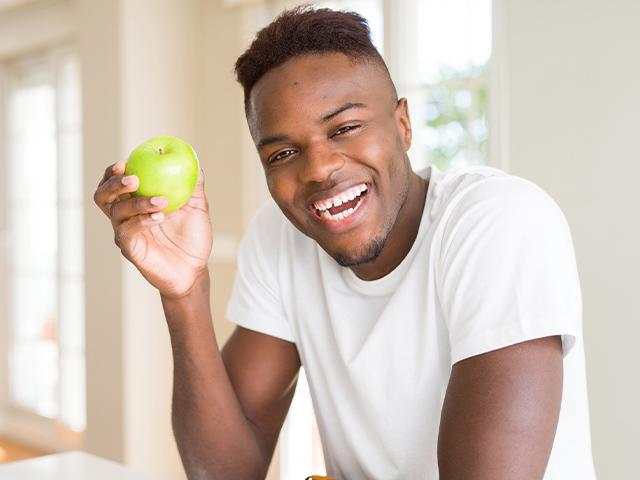 man smiling and holding up a green apple