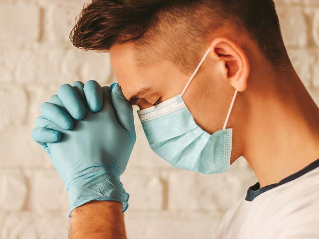young man praying while wearing surgical mask and gloves