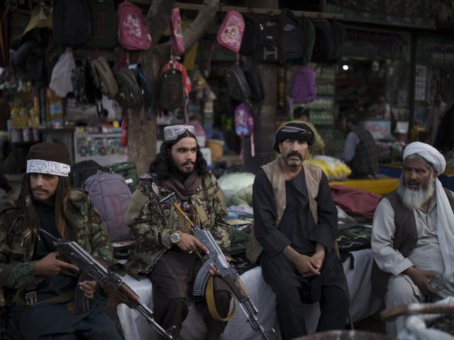 Taliban fighters sit next to street vendors at a local market in Kabul, Afghanistan