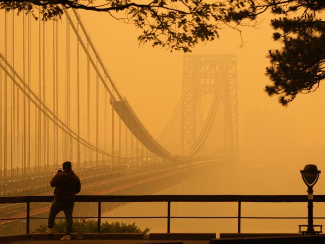 A man talks on his phone as he looks through the haze at the George Washington Bridge from Fort Lee, N.J., Wednesday, June 7, 2023. (AP Photo/Seth Wenig)
