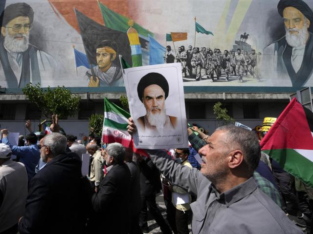 Iranian worshippers walk past a mural, as they hold posters of Ayatollah Khomeini and Iranian and Palestinian flags in an anti-Israeli gathering after Friday prayers in Tehran, Iran, April 19, 2024. (AP Photo/Vahid Salemi, File)