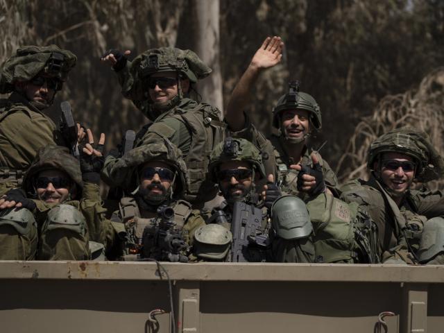 Israeli soldiers wave to the camera as they move on the back of a truck near the Israeli-Gaza border as seen from southern Israel, Monday, June 10, 2024. (AP Photo/Leo Correa)
