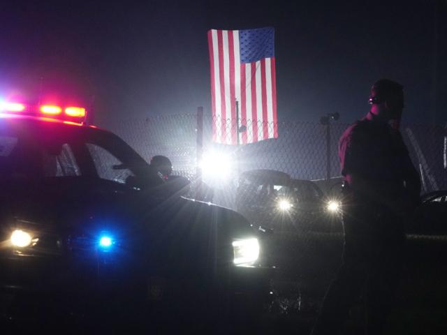 An officer stands at his car early Sunday, July 14, 2024, at the site of the rally where former President Donald Trump was the target of an assassination attempt in Butler, PA. A large flag from the rally still flies behind him. (AP Photo/Sue Ogrocki)