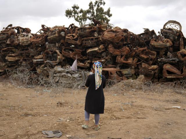 A woman looks at charred vehicles burned in the Oct. 7 cross-border attack by Hamas militants outside the town of Netivot, southern Israel, Monday, Oct. 7, 2024. (AP Photo/Ariel Schalit)