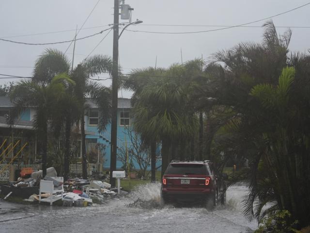 A car drives past a pile of debris from Hurricane Helene flooding, along a street that had already begun flooding from rain ahead of the arrival of Hurricane Milton, in Gulfport, Fla., Wednesday, Oct. 9, 2024. (AP Photo/Rebecca Blackwell)