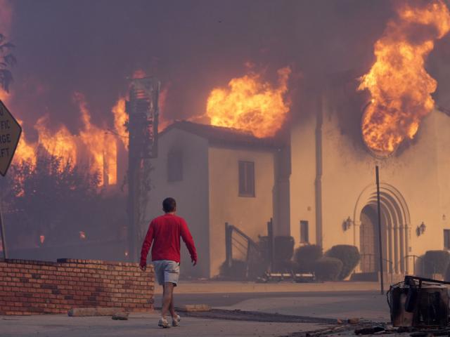 A man walks in front of the burning Altadena Community Church, Wednesday, Jan. 8, 2025, in the downtown Altadena section of Pasadena, Calif. (AP Photo/Chris Pizzello)