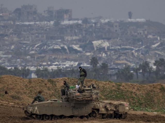 Destroyed buildings by Israeli bombardments inside the northern Gaza Strip can be seen as Israeli soldiers work on their tank in southern Israel, Tuesday, Feb.11, 2025. (AP Photo/Ariel Schalit)