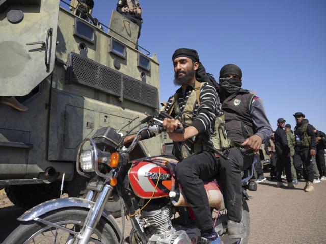 Two fighters from the Sunni Bedouin clans ride their motorcycle as they pass by Syrian government security forces where clashes erupted between Druze militias and Sunni Bedouin clans, southern Syria, July 14, 2025. (AP Photo/Malek Khattab)