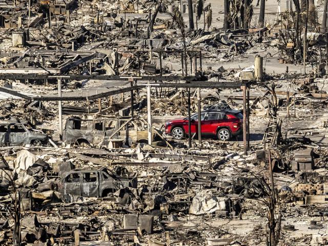 A car drives past homes and vehicles destroyed by the Palisades Fire at the Pacific Palisades Bowl Mobile Estates on Sunday, Jan. 12, 2025, in Los Angeles. (AP Photo/Noah Berger)