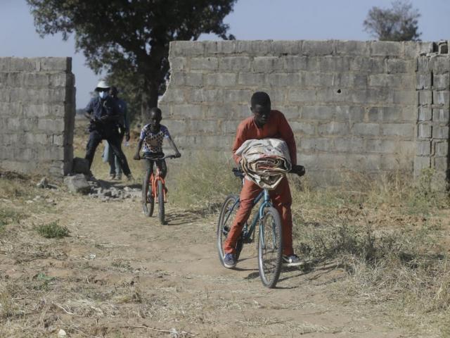 Image Source: Children ride on bicycles past a wall broken by Boko Haram who kidnapped students from their school (AP Photo/Sunday Alamba)