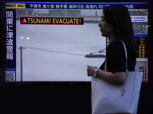 A pedestrian walks past a TV screen displaying a tsunami warning in Tokyo, Wednesday, July 30, 2025. (AP Photo/Louise Delmotte)