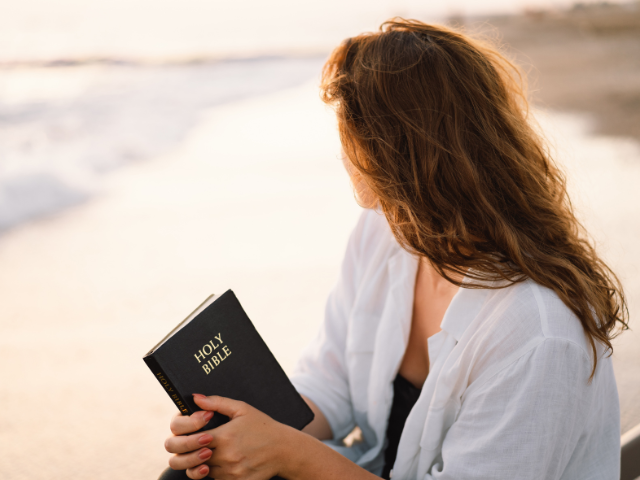 woman sitting beside the shoreline with her Bible