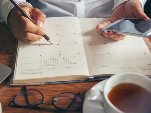 person writing on a calendar planner and holding a smartphone