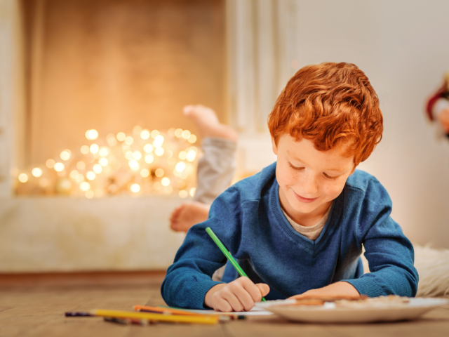 smiling child laying on the floor and coloring on paper