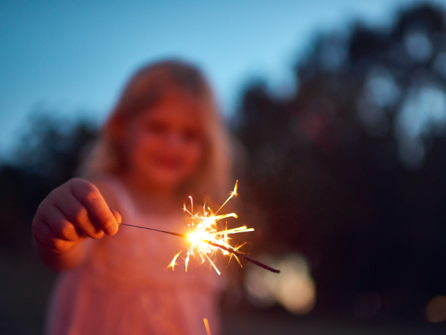 child holding a lit sparkler outside