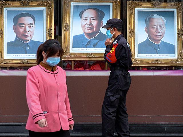 A security guard and worker walk past portraits of Chinese leaders, from left, Zhou Enlai, Mao Zedong, and Liu Shaoqi in the window of a photo studio in Beijing, April 15, 2020 (AP Photo/Mark Schiefelbein)