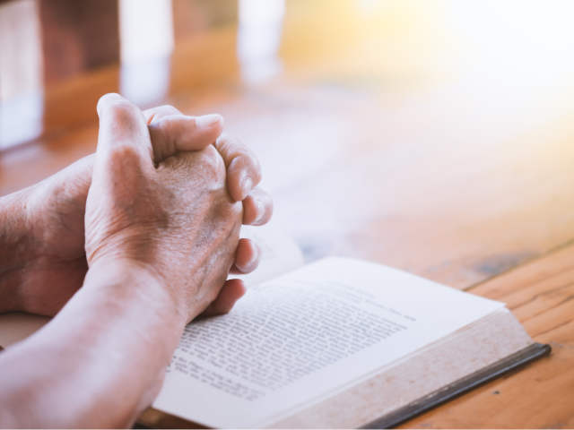 a man meditating with clasped hands over a book 