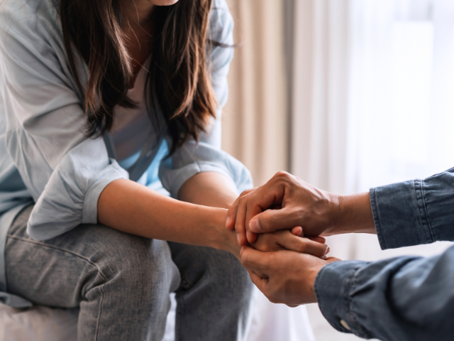 woman sitting across from a man who has reached out for her hands