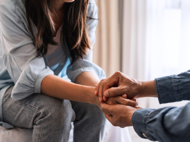 woman sitting across from a man who has reached out for her hands 