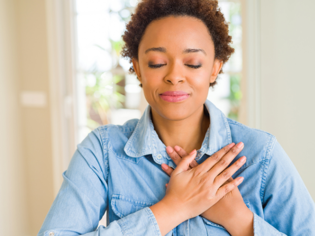 woman with eyes closed and smiling with hands over her heart