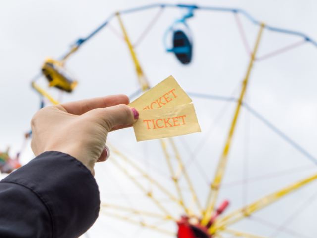 woman&#039;s hand holding up two tickets to the ferris wheel in the background