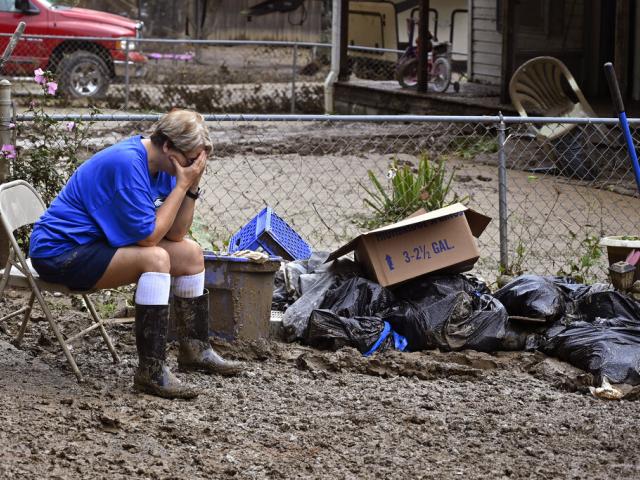 Teresa Reynolds sits exhausted as members of her community clean the debris from their flood ravaged homes in Ogden Hollar at Hindman, Ky., Saturday, July 30, 2022. (AP Photo/Timothy D. Easley)