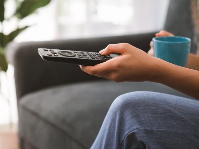Person with a cup of coffee and a remote control