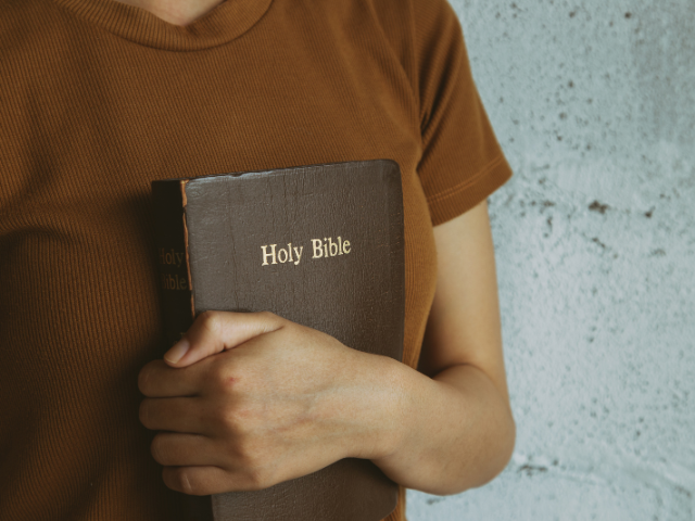 girl holding a closed Holy Bible in front of her