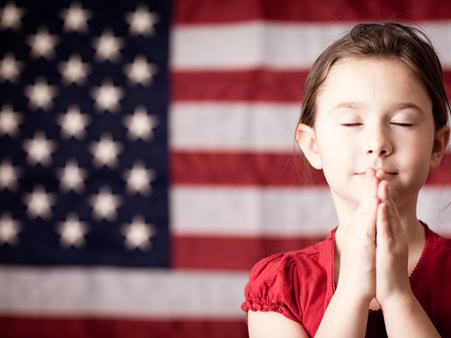 usa flag in the background and little girl praying with eyes closed