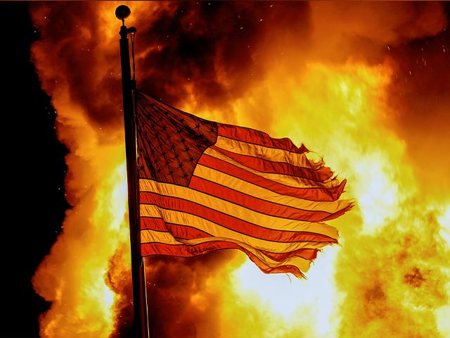A flag flies over a department of corrections building ablaze during protests on Aug. 24, 2020, in Kenosha, Wis. (AP Photo/Morry Gash)
