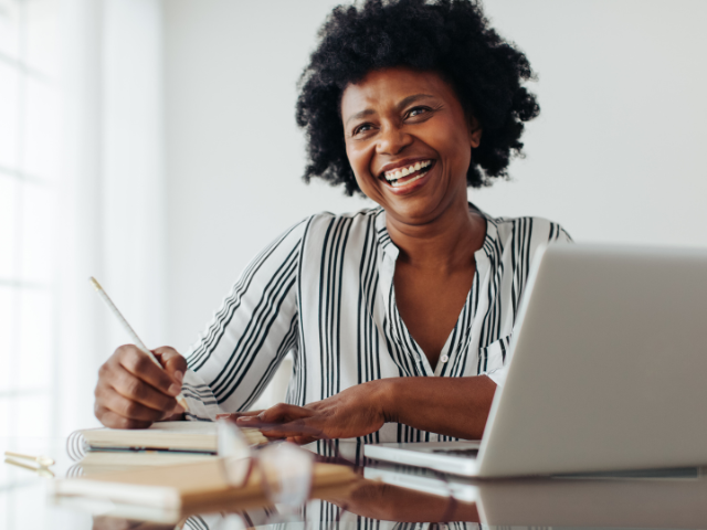 happy woman taking notes beside open laptop