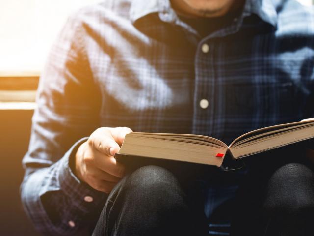 man reading a Bible near a window