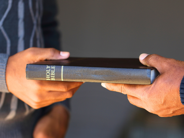 a man giving a Holy Bible to another man